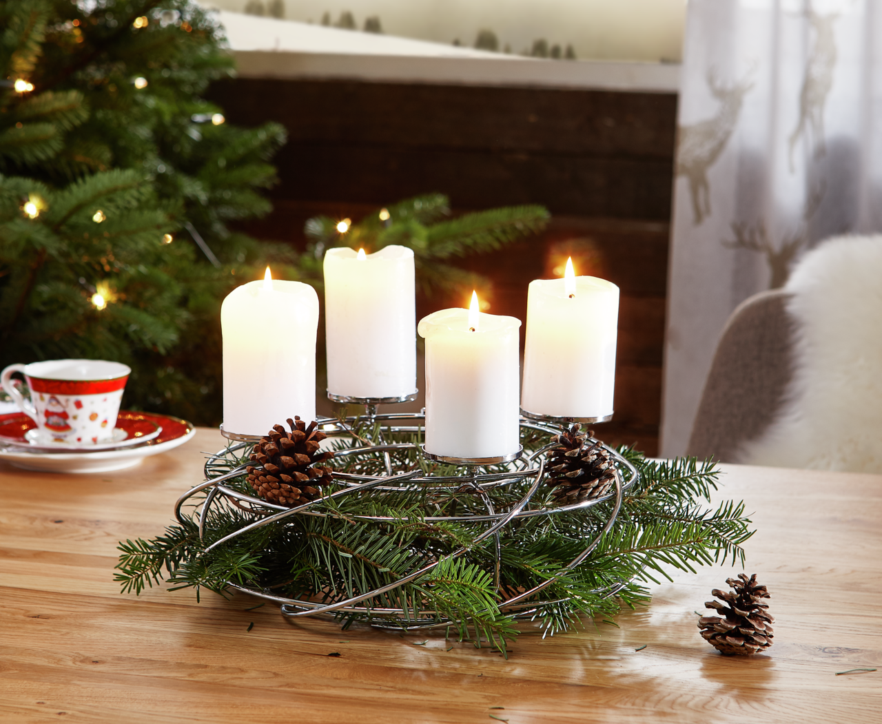 Silberner Dekokranz für 4 Kerzen mit Tannenzweigen und Zapfen, auf einem Tisch in weihnachtlicher Umgebung, seitliche Perspektive