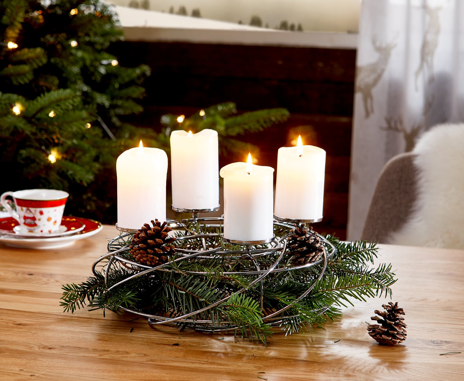 Silberner Dekokranz für 4 Kerzen mit Tannenzweigen und Zapfen, auf einem Tisch in weihnachtlicher Umgebung, seitliche Perspektive