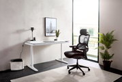 Moderner weißer E-Schreibtisch in einem hellen Raum, seitliche Perspektive, mit einem ergonomischen schwarzen Bürostuhl und einer Pflanze im Hintergrund.
