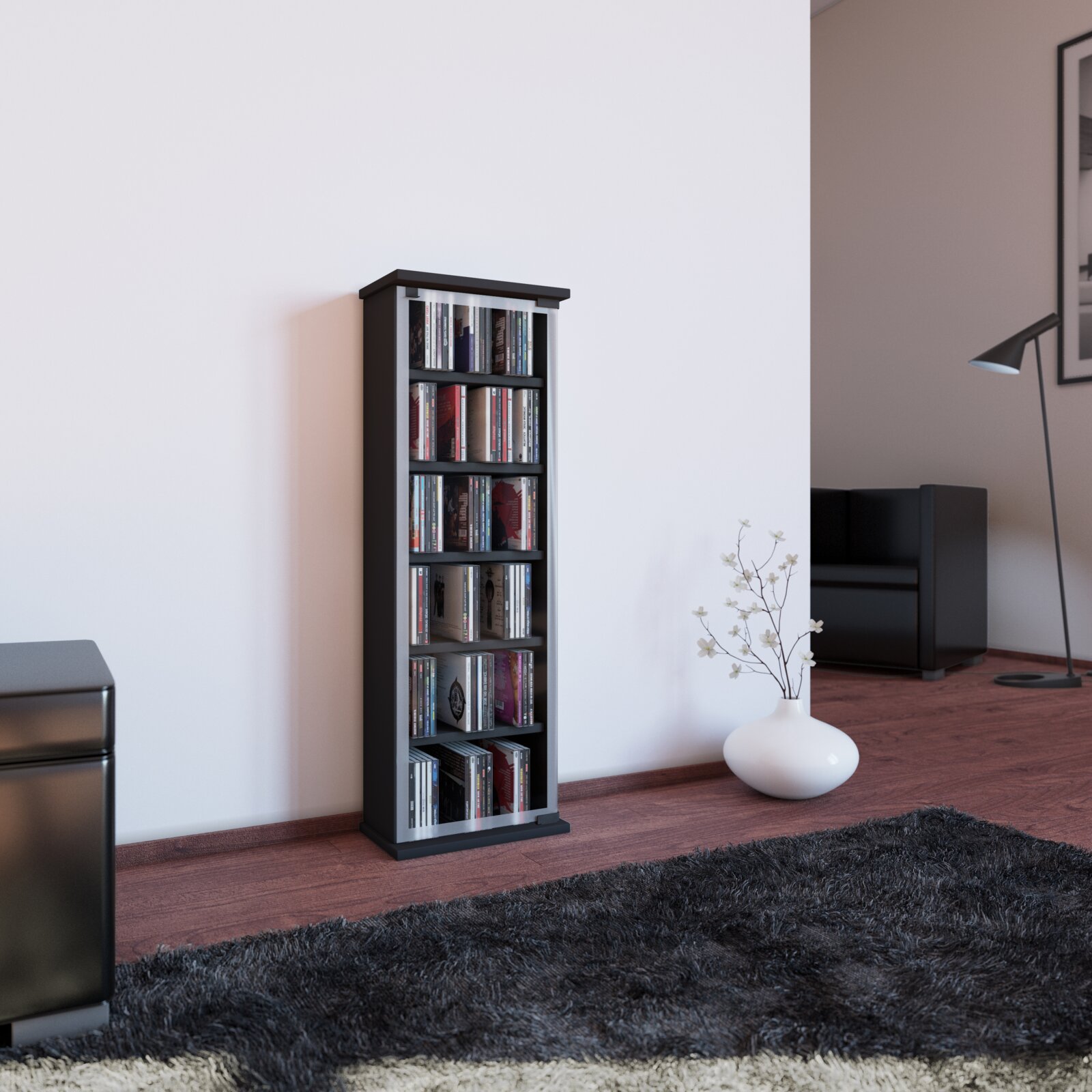 Schmales schwarzes CD-/DVD-Regal mit mehreren Fächern, gefüllt mit Medienhüllen, im Wohnzimmer an einer weißen Wand Perspektive: leicht schräg von vorn aus Augenhöhe.
