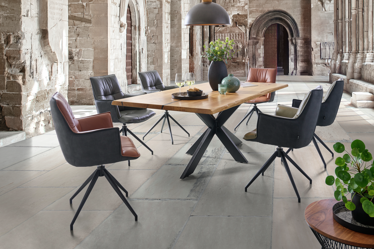 Linea Natura Esstisch 220x100 HERO Moderner Esstisch mit Holzplatte und Metallgestell, umgeben von stilvollen Drehstühlen in einem historischen Raum, seitliche Perspektive.