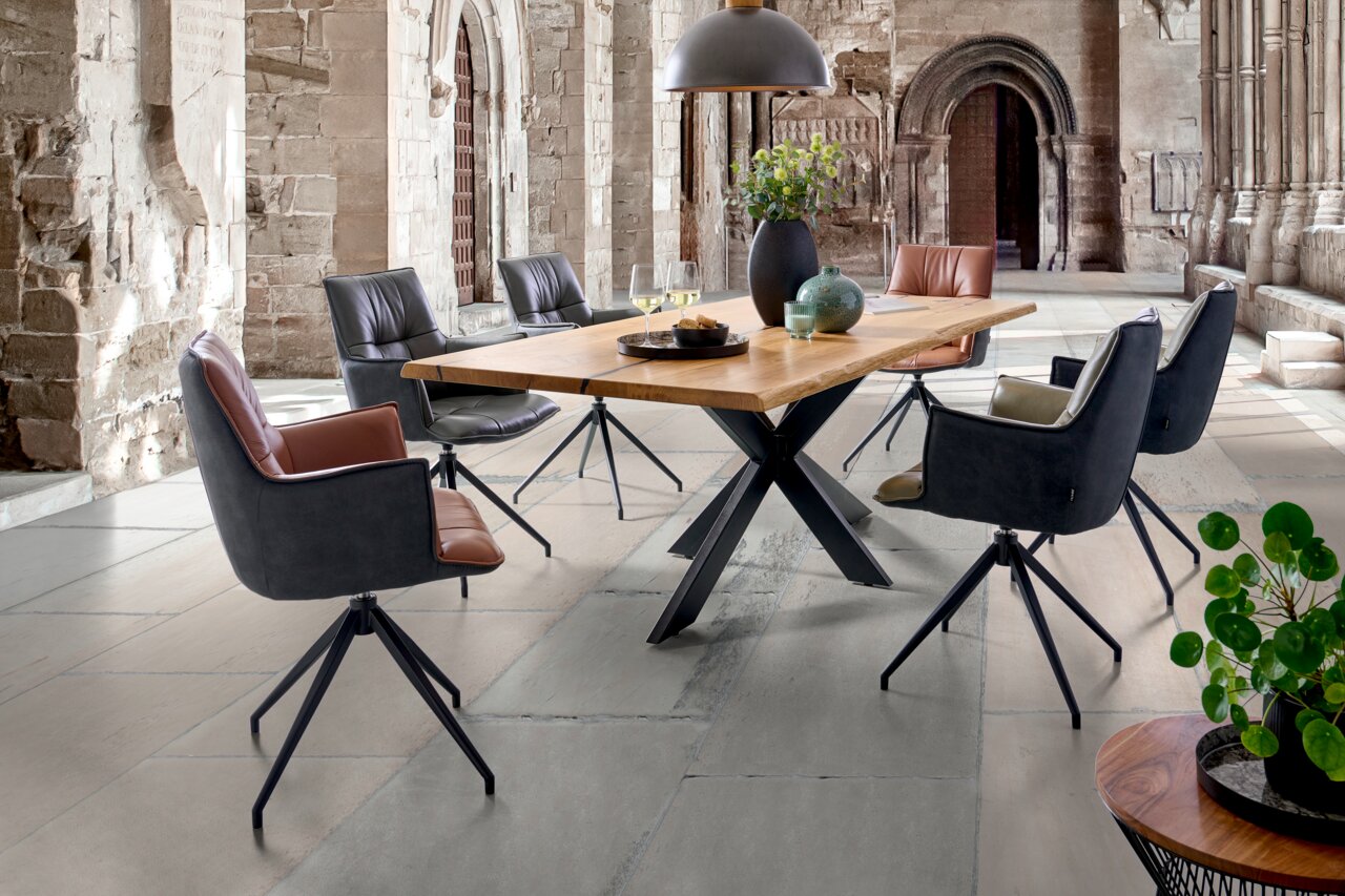 Linea Natura Esstisch 220x100 HERO Moderner Esstisch mit Holzplatte und Metallgestell, umgeben von stilvollen Drehstühlen in einem historischen Raum, seitliche Perspektive.