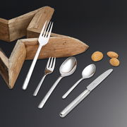 Elegantes Besteckset Viva 60-tlg. aus Edelstahl, bestehend aus Messer, Gabel, Löffel und Teelöffel, auf schwarzem Hintergrund mit Holzstern und Mandeln, aus der Vogelperspektive.