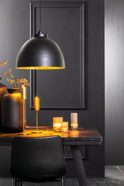 Schwarze Hängeleuchte KYLIE mit goldener Innenseite, über einem Tisch mit Kerzen und Dekorationen, seitliche Perspektive.