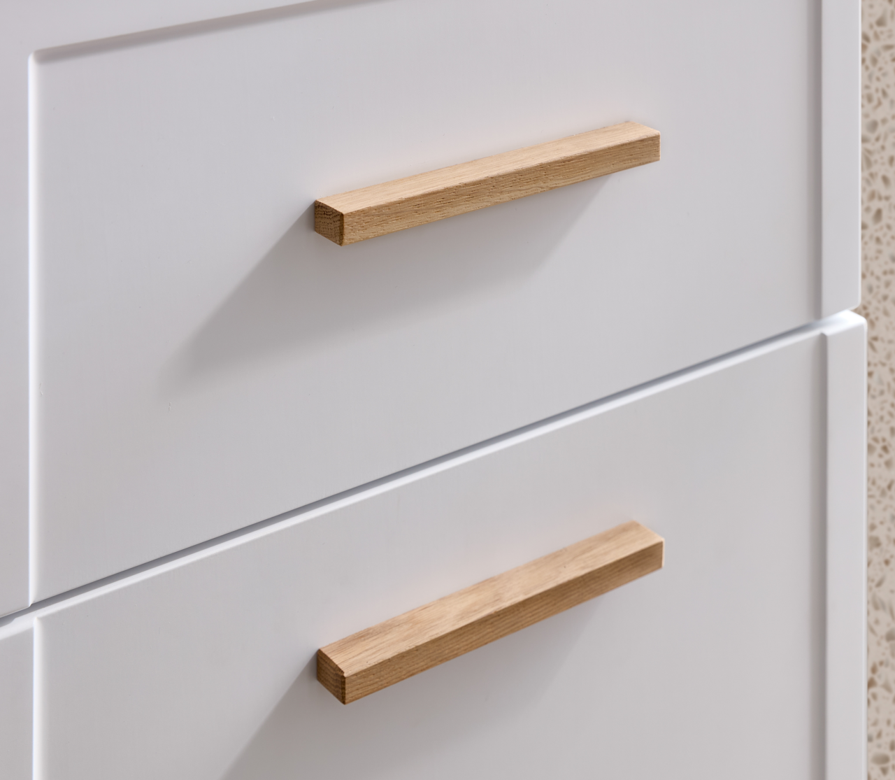 Nahaufnahme eines weißen Unterschranks mit zwei Schubladen und Holzgriffen, seitliche Perspektive