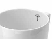 Nahaufnahme eines weißen Bechers mit Henkel, verziert mit einem kleinen schwarzen Symbol im Inneren. Perspektive von oben.