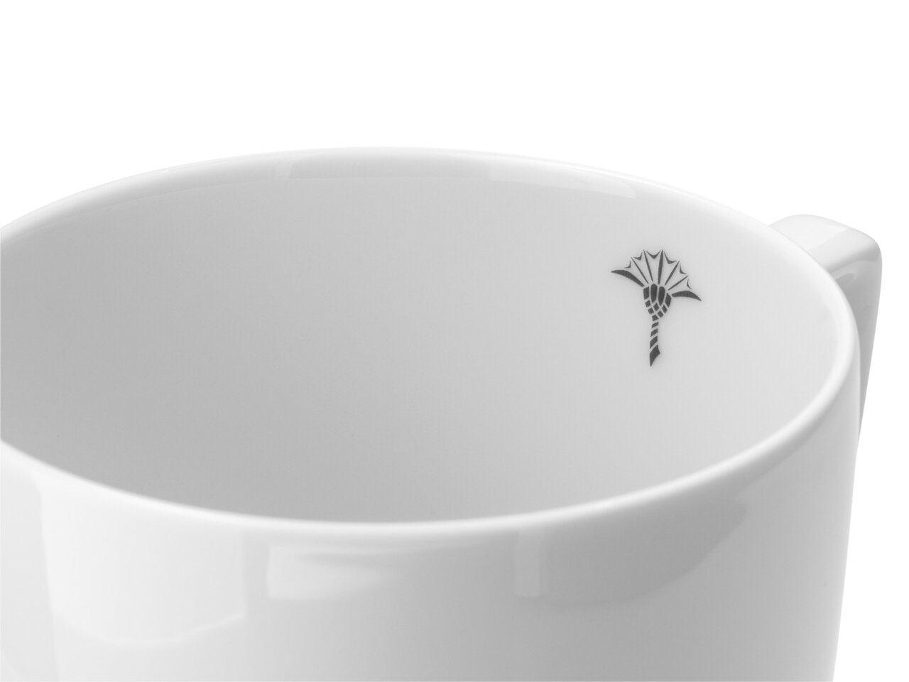 Nahaufnahme eines weißen Bechers mit Henkel, verziert mit einem kleinen schwarzen Symbol im Inneren. Perspektive von oben.