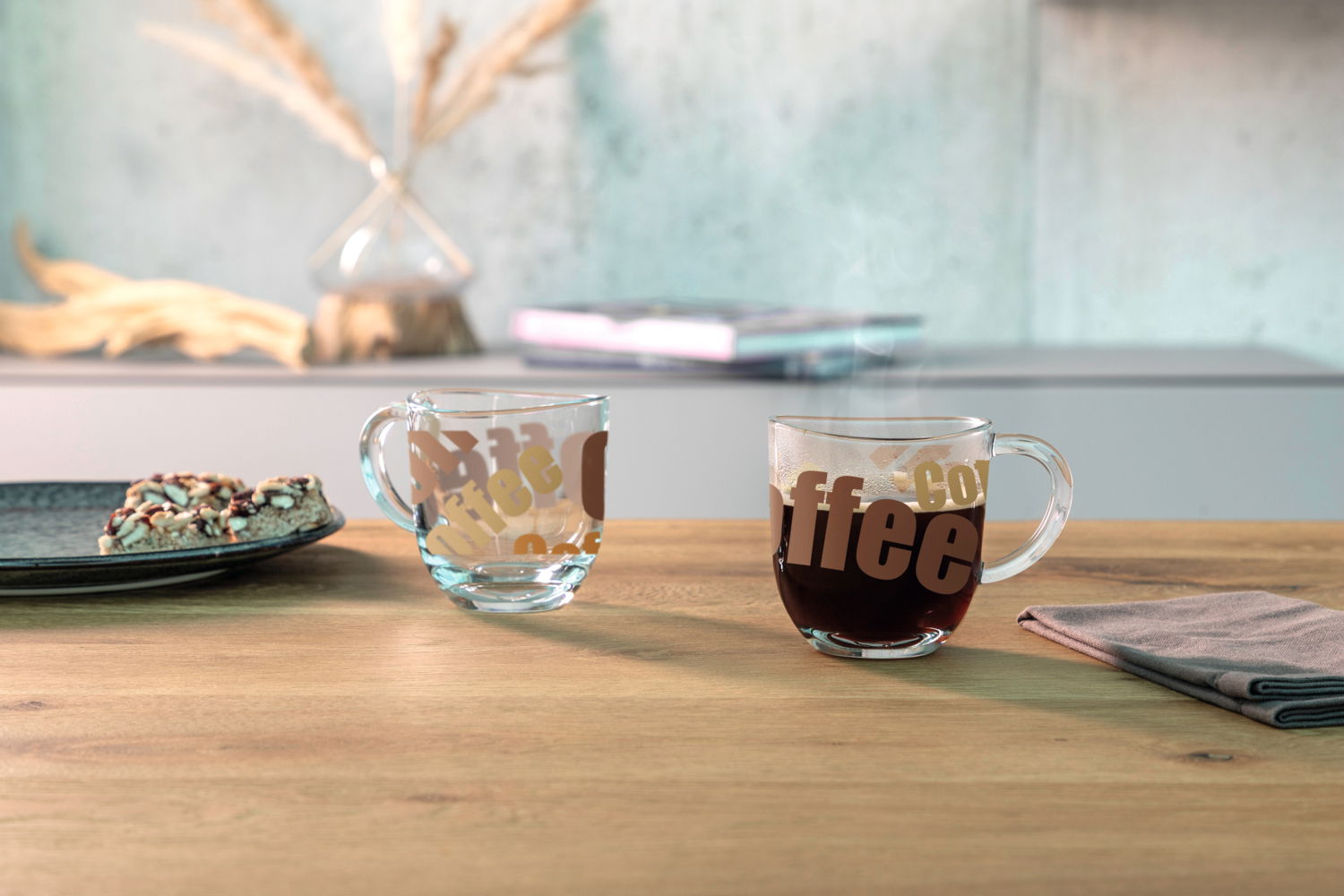 Leonardo Kaffeetasse NAPOLI Zwei durchsichtige Tassen mit dem Aufdruck 'Coffee' auf einem Holztisch, eine mit schwarzem Kaffee gefüllt, die andere leer, im Hintergrund unscharfe Dekoration und Bücher, seitliche Perspektive.