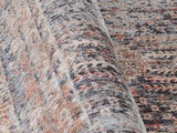 Nahaufnahme eines Frisé-Teppichs mit gemustertem Design in verschiedenen Grautönen und Rottönen, aus seitlicher Perspektive aufgenommen.