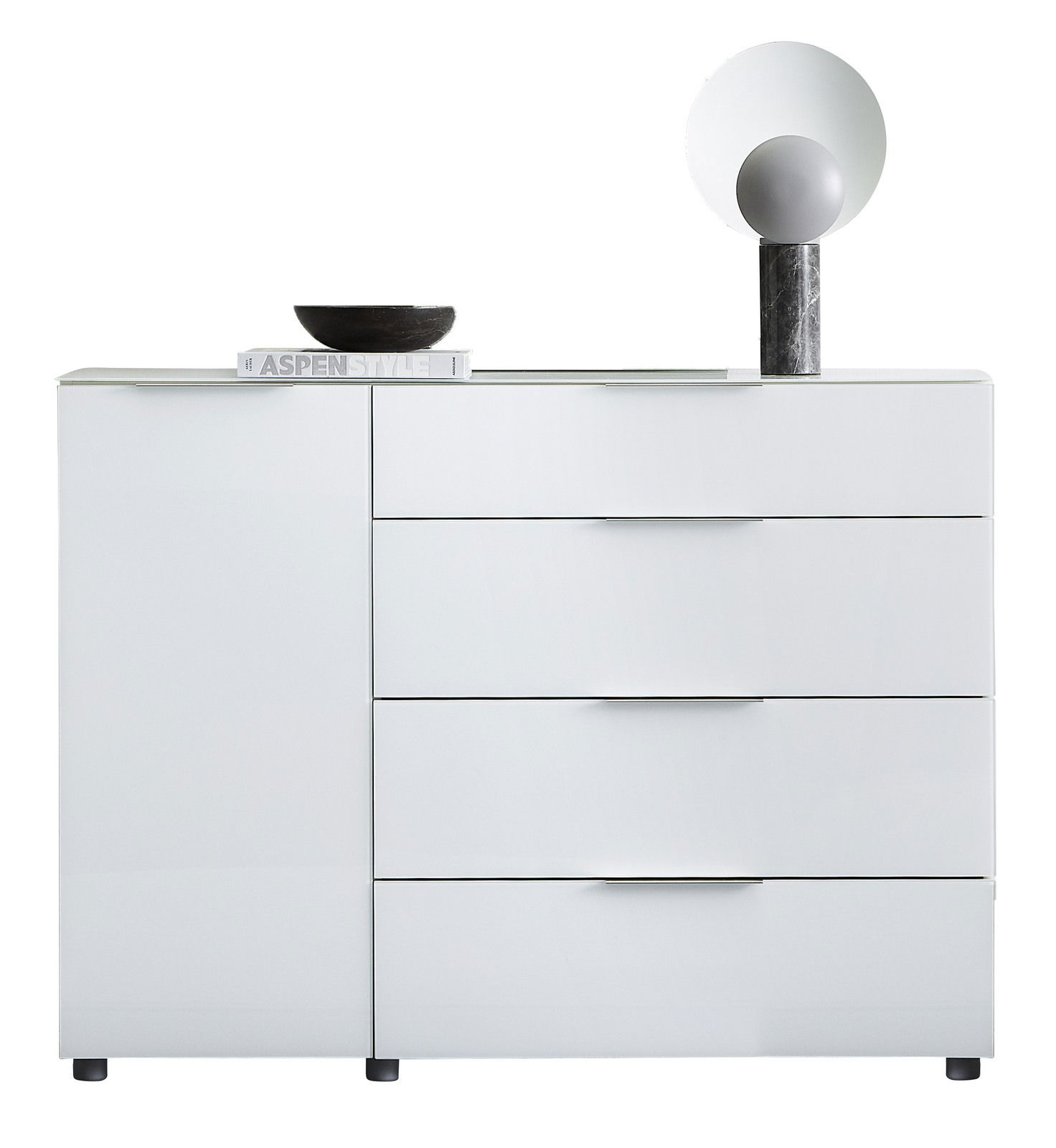 Weiße Kombikommode mit drei Schubladen und einer Tür, frontal fotografiert. Dekoriert mit einer schwarzen Schale, einem Buch und einer modernen Lampe.