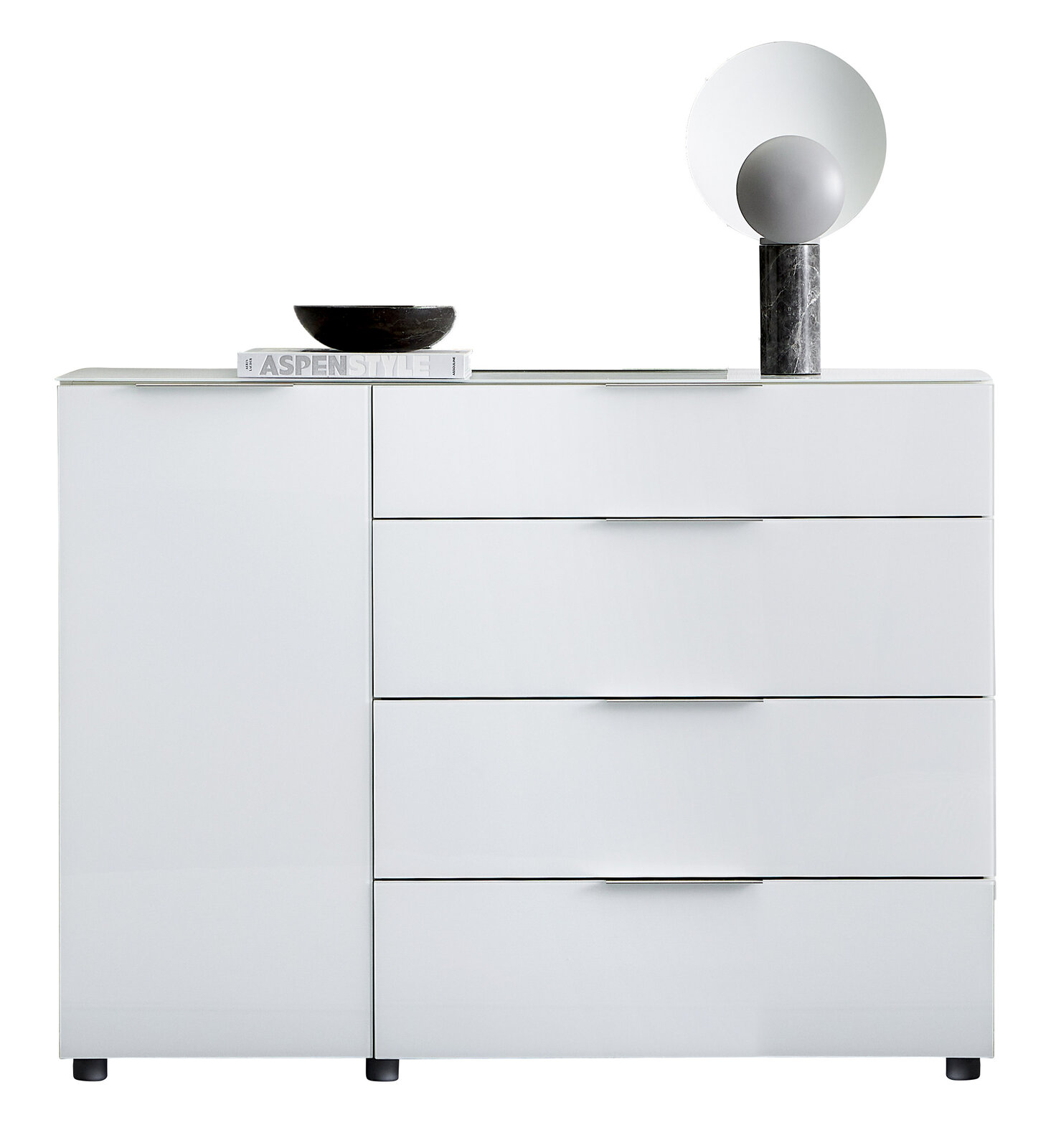 Weiße Kombikommode mit drei Schubladen und einer Tür, frontal fotografiert. Dekoriert mit einer schwarzen Schale, einem Buch und einer modernen Lampe.