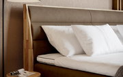 Nahaufnahme eines Boxspringbettes mit braunem Kopfteil und weißen Kissen, seitliche Perspektive
