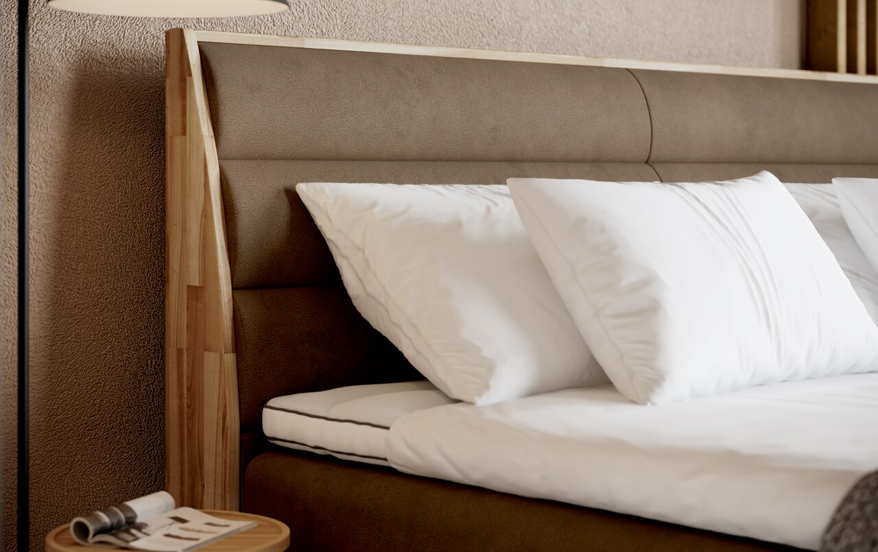 Nahaufnahme eines Boxspringbettes mit braunem Kopfteil und weißen Kissen, seitliche Perspektive