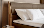 Close-up van een boxspringbed met een bruin hoofdeinde en witte kussens, gezien vanaf de zijkant
