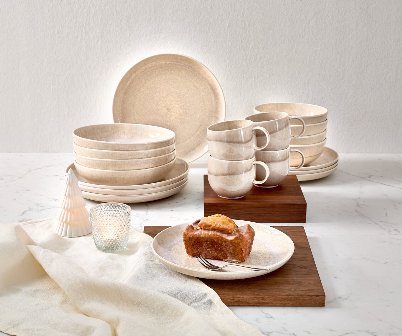Frühstücksservice 12-tlg. in natürlichem Beige-Ton, bestehend aus Tellern, Schalen und Tassen, auf einem Tisch mit Holzuntersetzern und Dekoration. Perspektive: Frontalansicht.