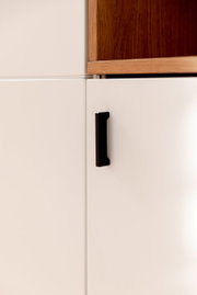 Nahaufnahme eines Highboards mit weißer Tür und schwarzem Griff, obere Ecke aus Holz, seitliche Perspektive