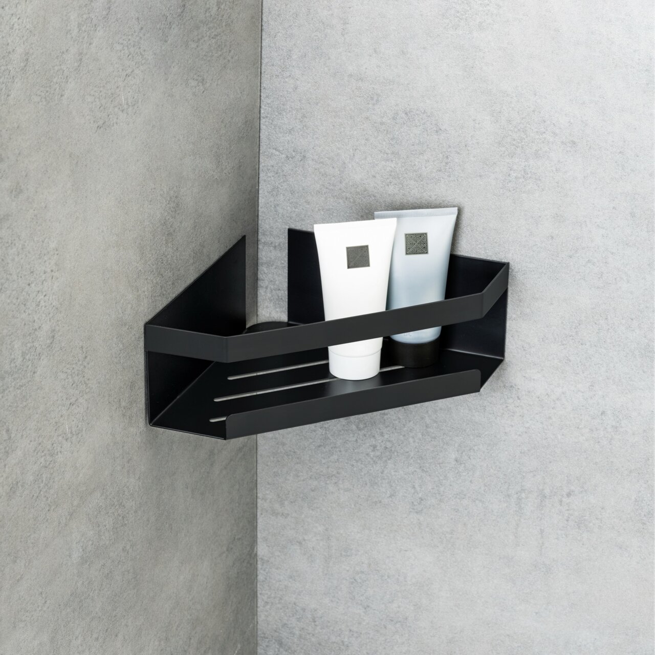 Schwarze Eckablage Meleto an einer grauen Wand montiert, mit zwei Tuben darauf, seitliche Perspektive.