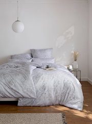 Bettwäsche GREGORIO in einem hellen Schlafzimmer, frontal fotografiert, mit elegantem Muster und dekorativen Kissen.