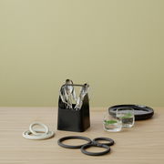 Schwarze Aufbewahrungsbox mit Besteck, von vorne gesehen, auf einem Holztisch mit weiteren Küchenutensilien.