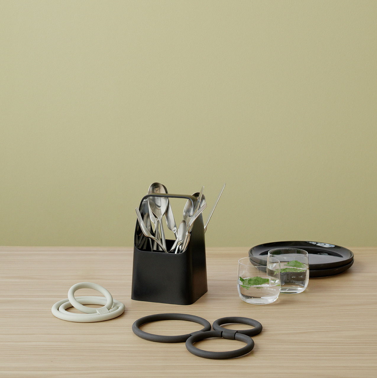 Schwarze Aufbewahrungsbox mit Besteck, von vorne gesehen, auf einem Holztisch mit weiteren Küchenutensilien.