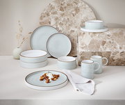 Kombiservice 10-tlg. in sanftem Blau mit braunem Rand, bestehend aus Tellern, Schalen und Tassen, auf einer hellen Oberfläche mit dekorativem Hintergrund, seitliche Perspektive.