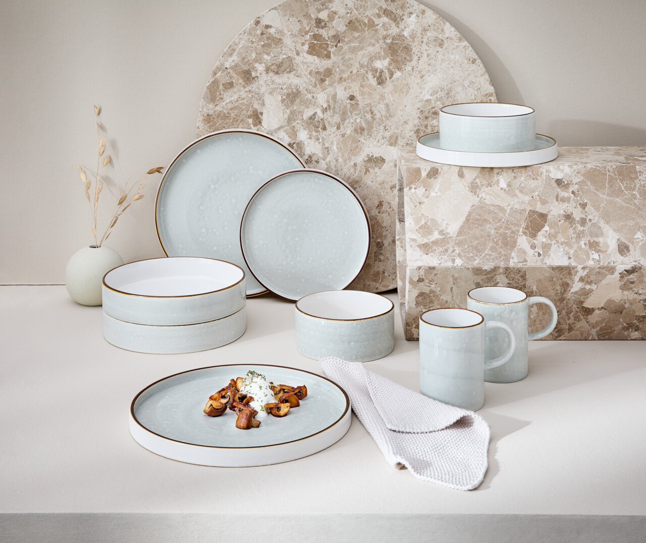 Kombiservice 10-tlg. in sanftem Blau mit braunem Rand, bestehend aus Tellern, Schalen und Tassen, auf einer hellen Oberfläche mit dekorativem Hintergrund, seitliche Perspektive.