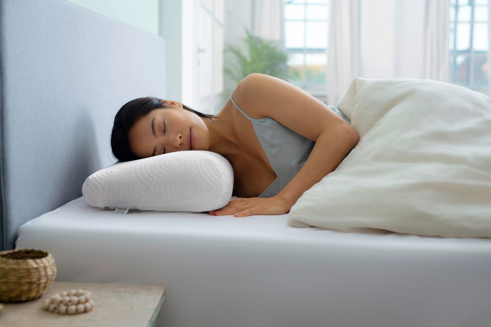 Frau schläft seitlich auf einem ergonomischen Schlafkissen in einem hellen Schlafzimmer.