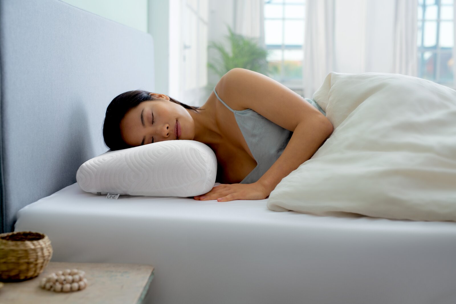 Een vrouw ligt op haar zij op een ergonomisch kussen in een lichte slaapkamer.