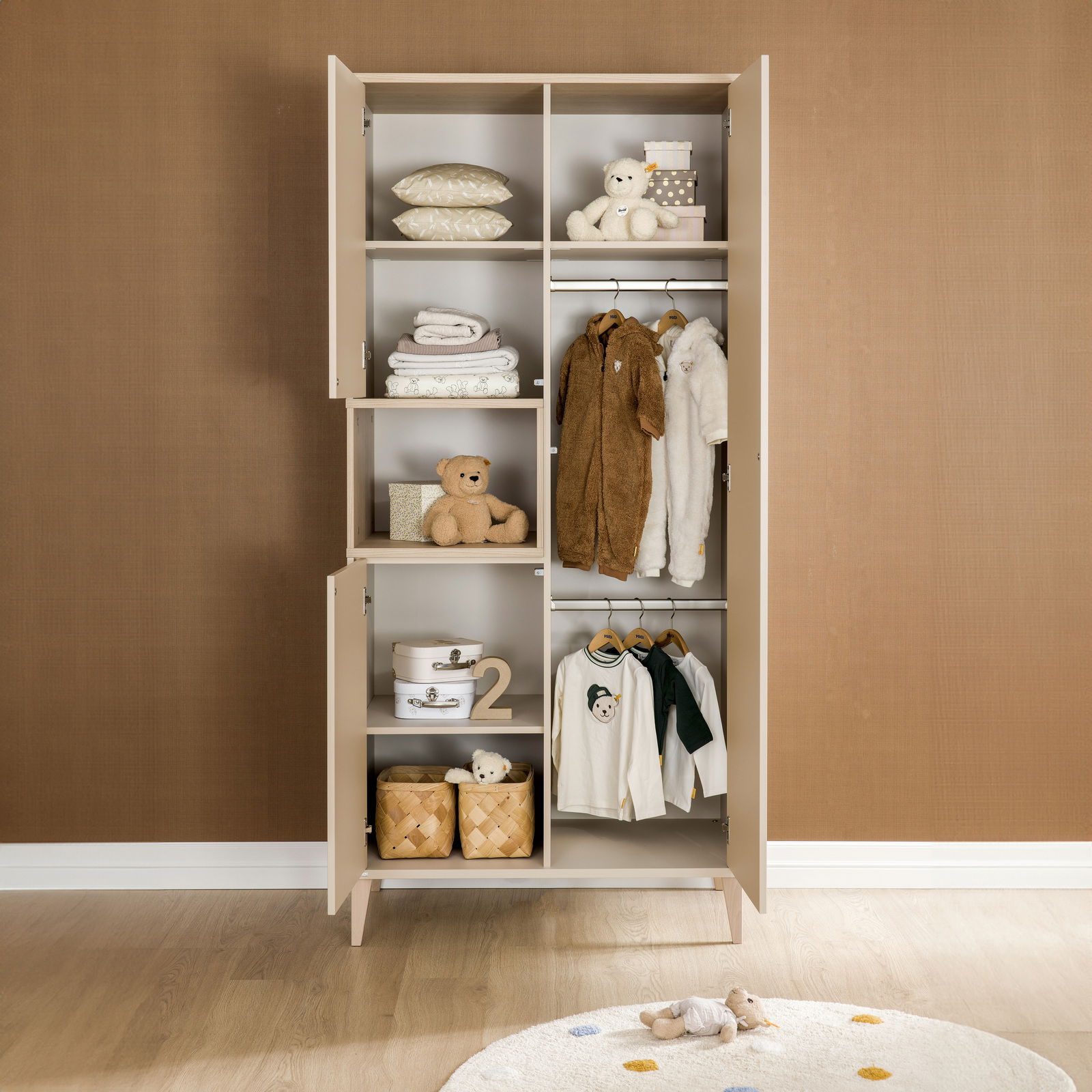 Offener dreitüriger Kleiderschrank mit Kinderkleidung, Spielzeug und Körben, frontal fotografiert.