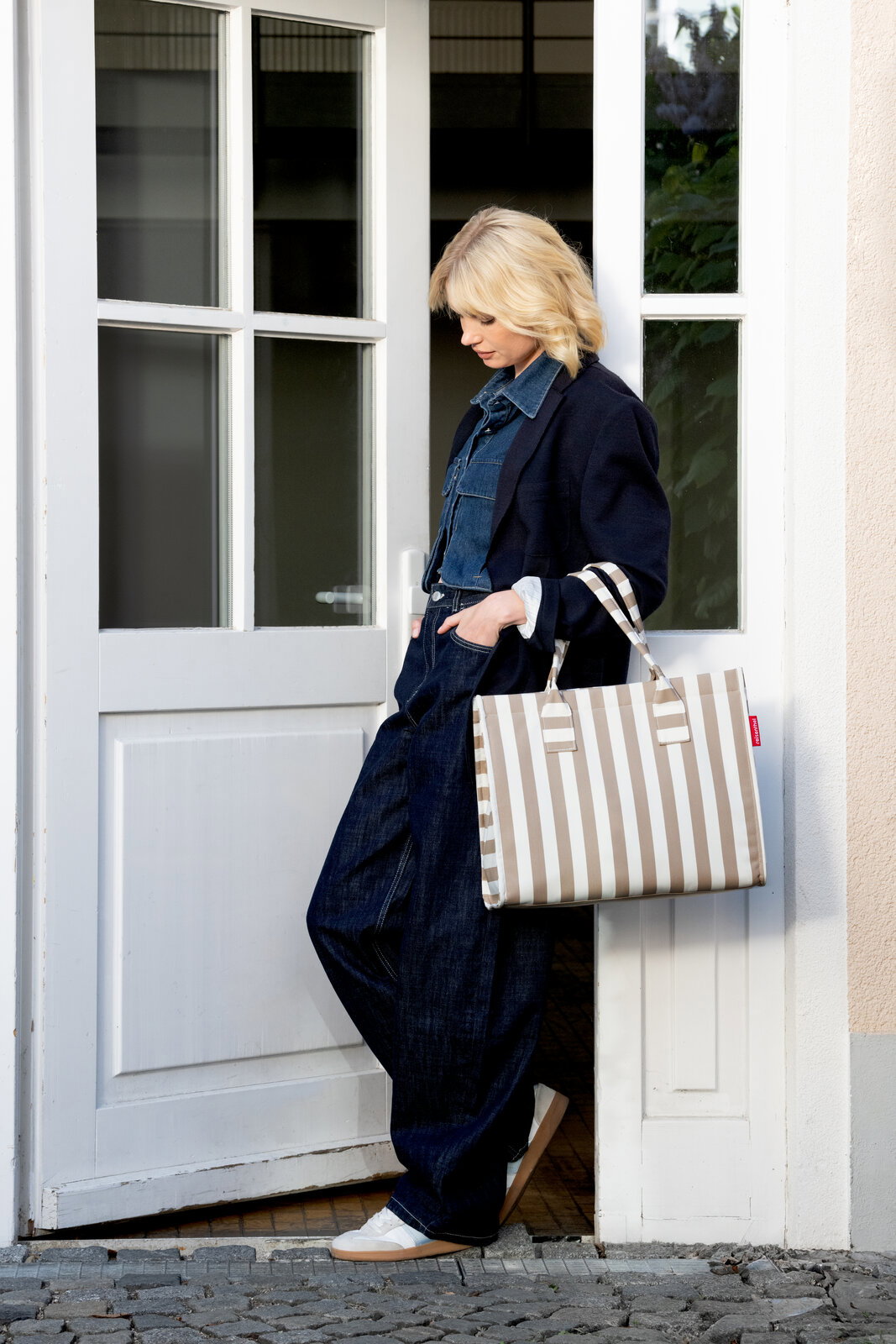 Beige-weiß gestreifte Shopper-Tasche mit langen Henkeln, seitliche Ansicht in Alltagsszene an einer Tür getragen