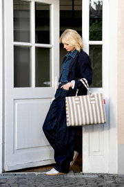 Beige-weiß gestreifte Shopper-Tasche mit langen Henkeln, seitliche Ansicht in Alltagsszene an einer Tür getragen