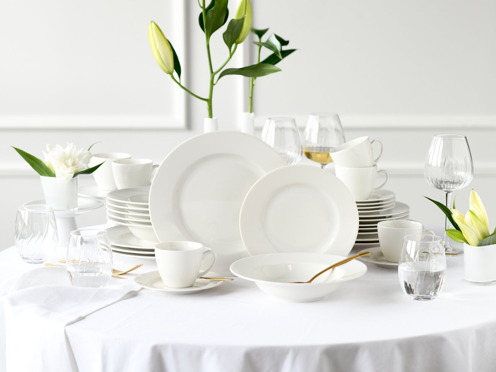 Creatable Kombiservice 30-tlg VENICE Weißes Porzellan-Geschirrset mit Tellern, Schalen und Tassen auf gedecktem Tisch mit Gläsern und Blumen, frontale Perspektive leicht von oben