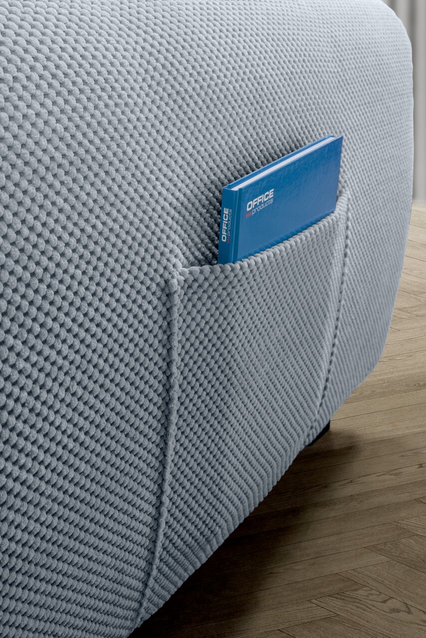 Nahaufnahme einer strukturierten, hellgrauen Sofaecke mit einer integrierten Tasche, die ein blaues Buch enthält, auf einem Holzboden.