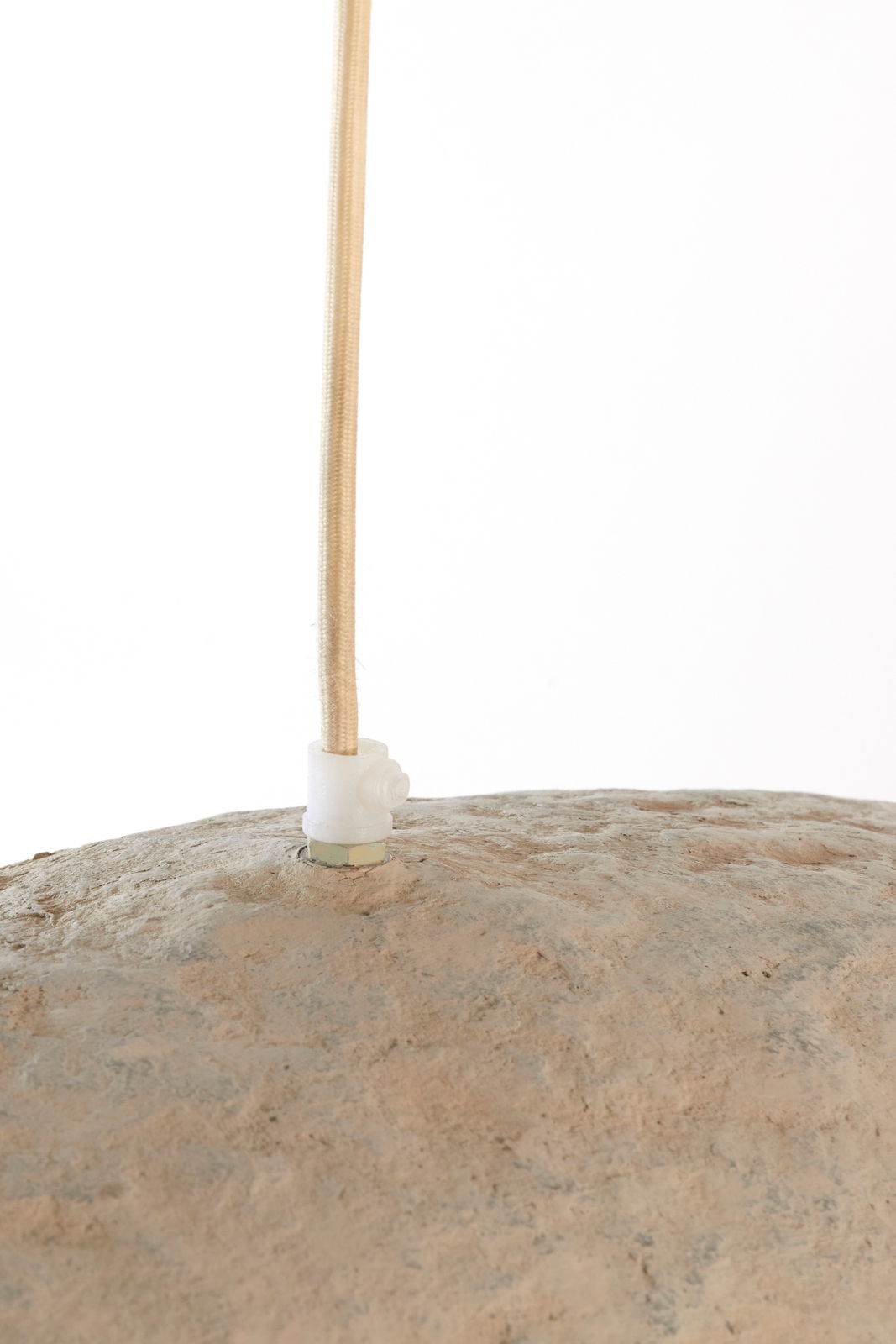 Nahaufnahme einer Hängeleuchte mit natürlicher, steinartiger Oberfläche und einem beige ummantelten Kabel von oben.