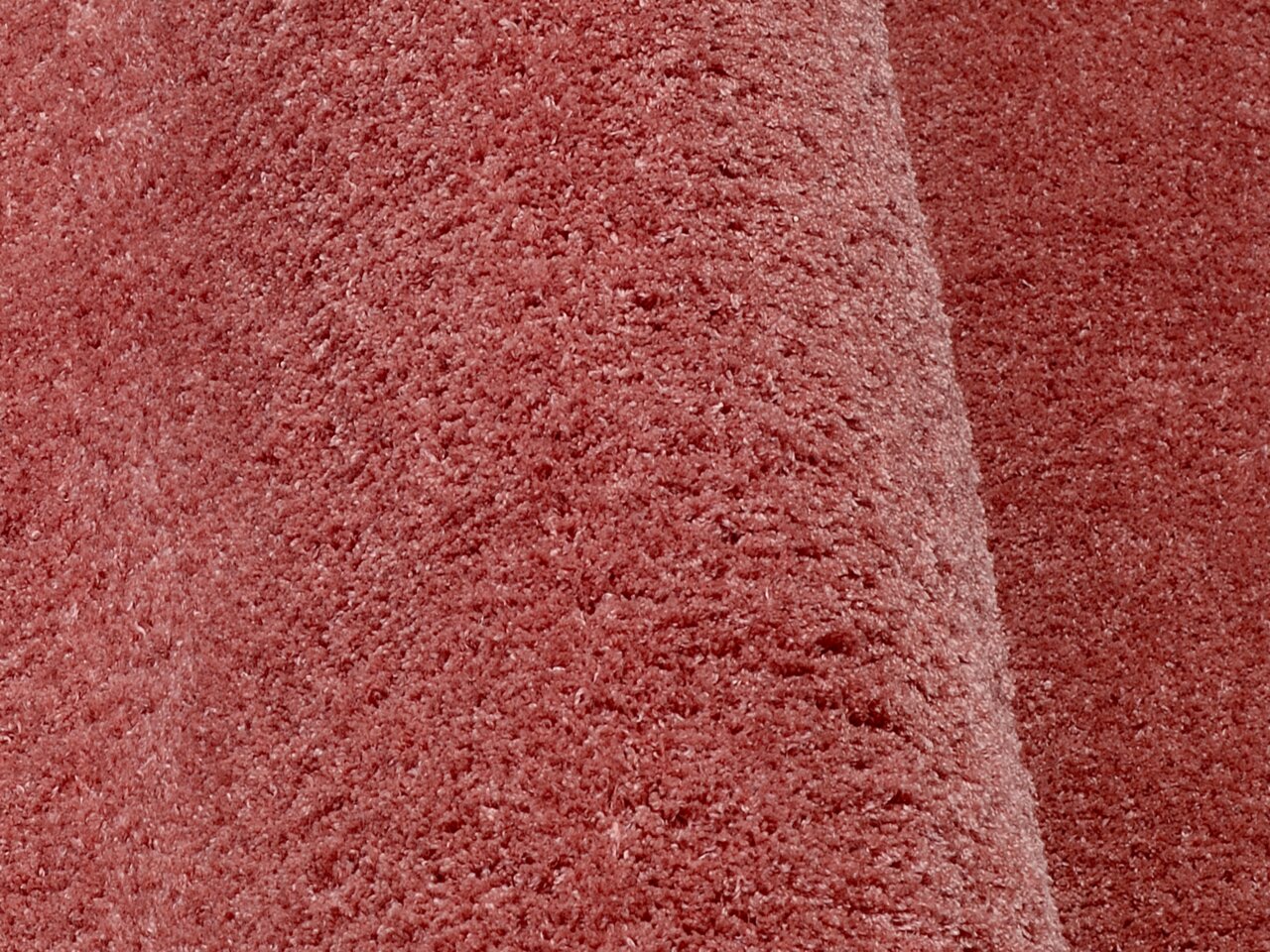 Nahaufnahme eines weichen, rosafarbenen Teppichs mit flauschiger Textur, perspektivisch von der Seite aufgenommen.