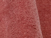 Nahaufnahme eines weichen, rosafarbenen Teppichs mit flauschiger Textur, perspektivisch von der Seite aufgenommen.