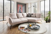 Moderne Longchairkombination in einem hellen Wohnzimmer mit großen Fenstern, einem runden Teppich und einem Couchtisch. Perspektive von vorne links.