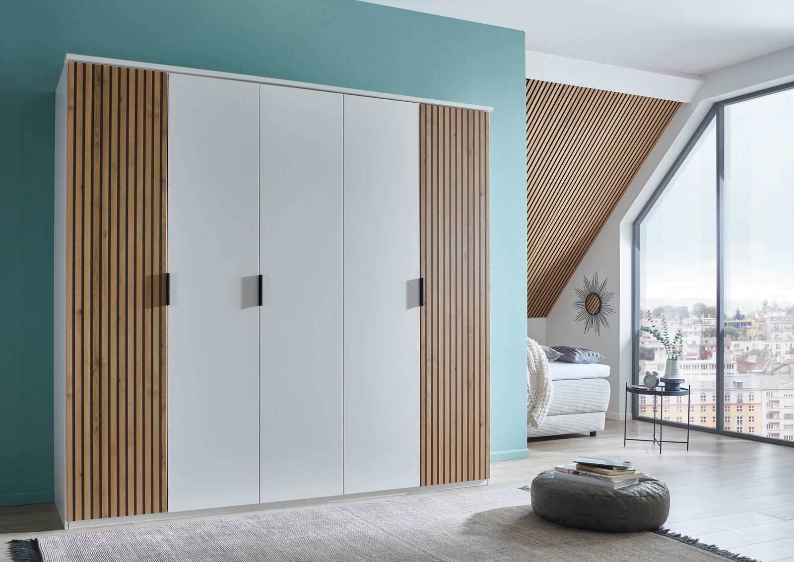 Moderner 5-türiger Drehtürenschrank mit weißen Fronten und Holzlamellen an den Seiten, in einem stilvoll eingerichteten Raum mit Blick auf ein großes Fenster. Perspektive von vorne links.