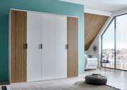 Moderne vijfdeurs draaideurkast met witte fronten en houten lamellen aan de zijkanten, in een stijlvol ingerichte ruimte met uitzicht op een groot raam. Aanzicht van linksvoor.