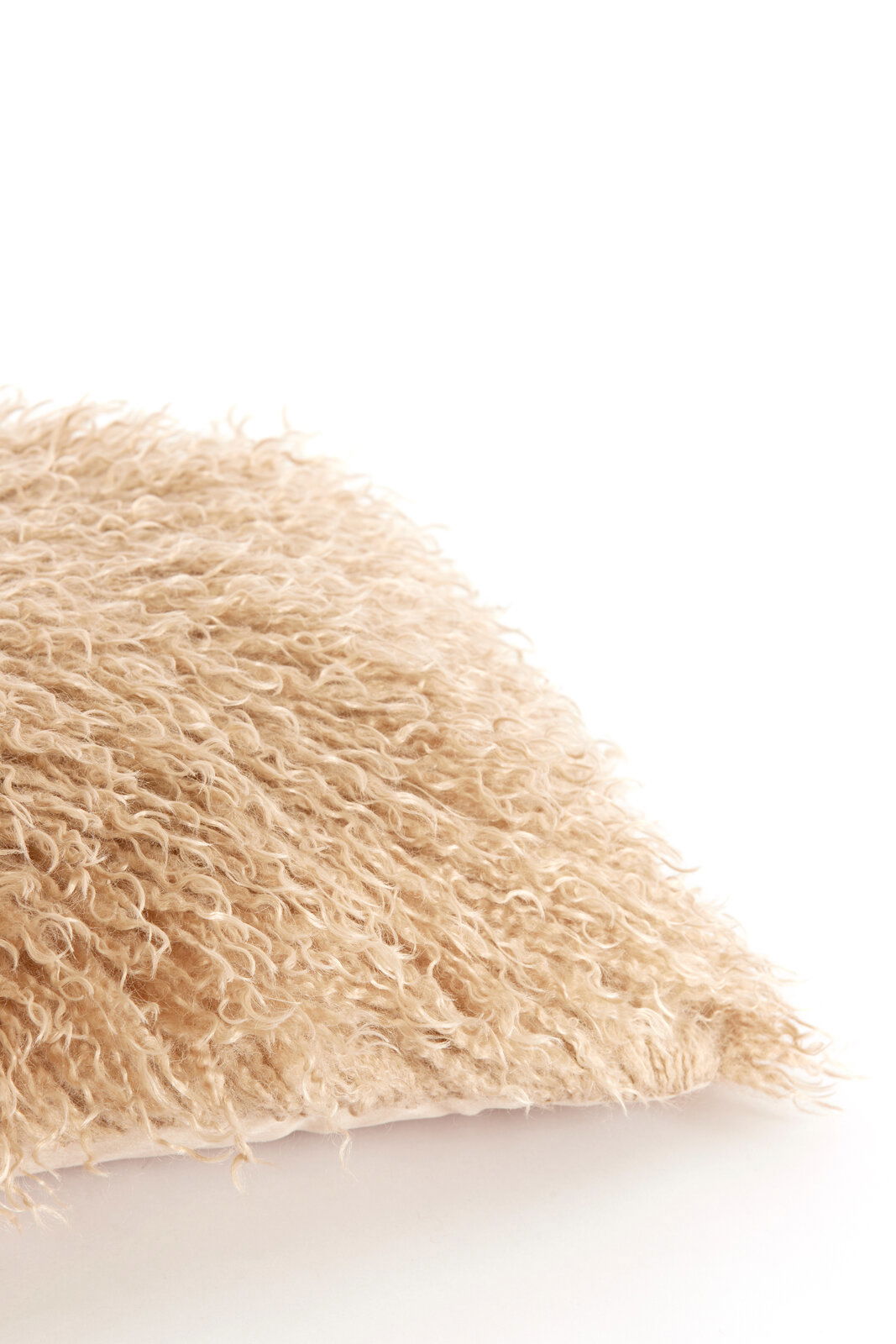 Nahaufnahme eines beigen, flauschigen Kissens mit langem Flor, von der Seite fotografiert.