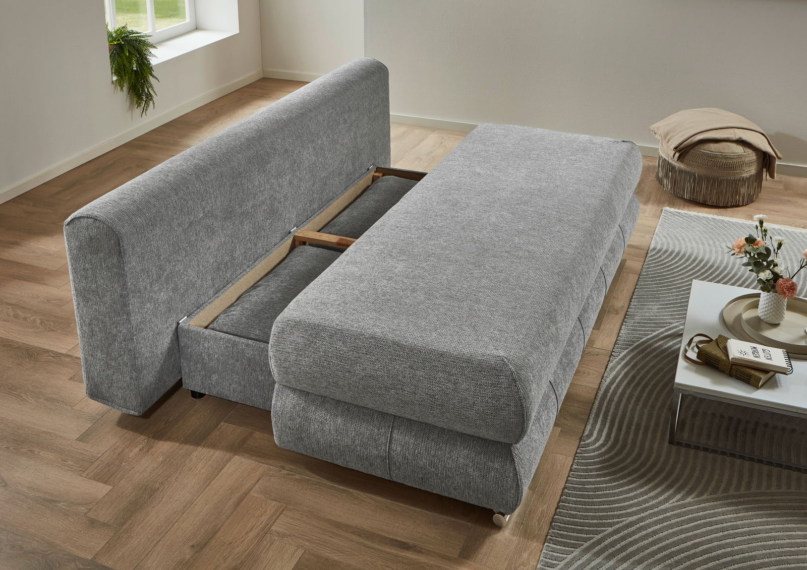 Graues Funktionssofa in ausgeklappter Position, seitliche Perspektive, auf einem Holzboden mit modernem Dekor.