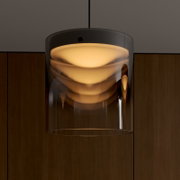 Moderne Pendelleuchte mit transparentem, zylindrischem Glasschirm und warm leuchtendem Diffusor, frontale Nahaufnahme von leicht unten