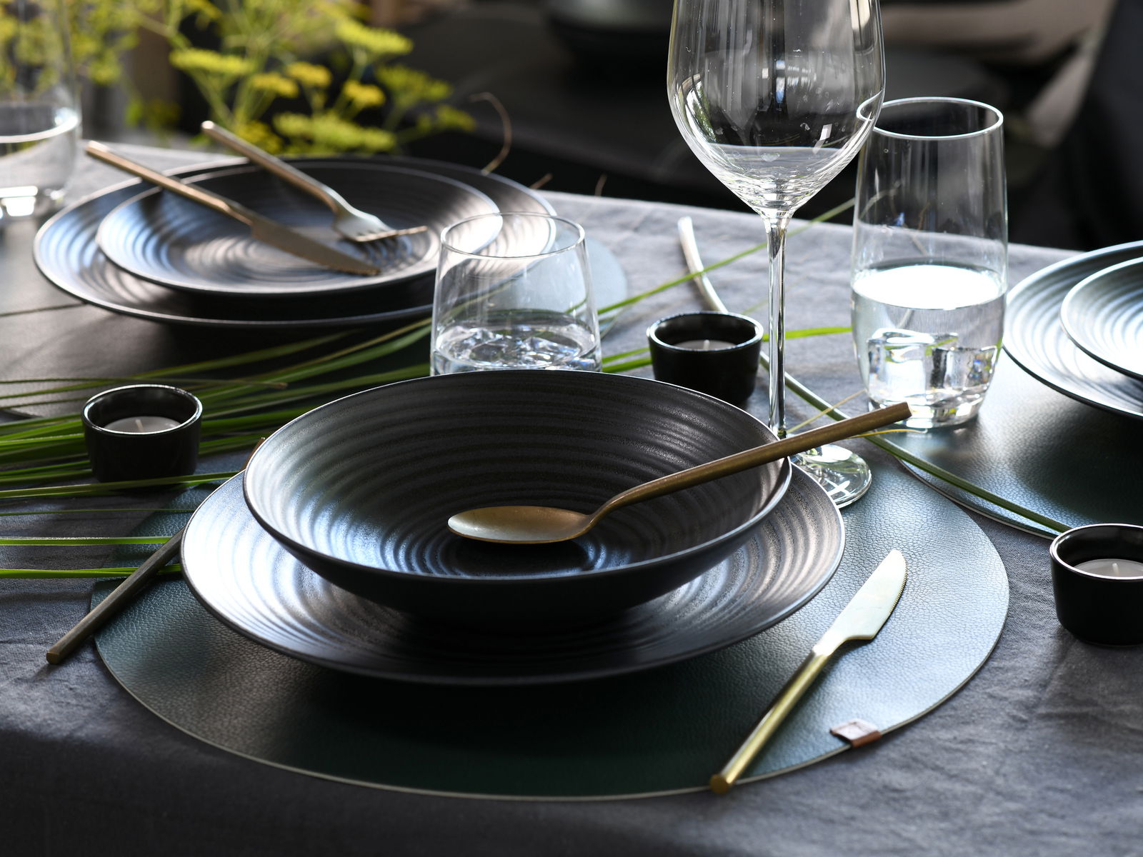 Elegantes Kombiservice 24-tlg in Schwarz mit goldfarbenem Besteck, stilvoll auf einem gedeckten Tisch arrangiert, seitliche Perspektive.