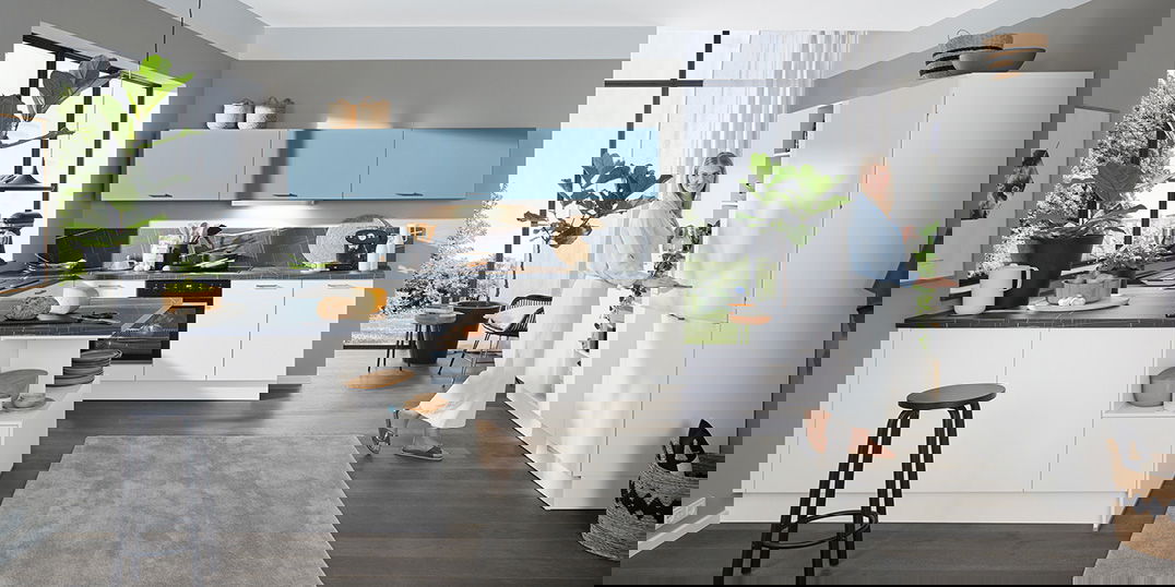 Helle, moderne Küche mit weißen Unterschränken, himmelblauen Oberschränken, dunkler Arbeitsplatte und großen Fensterfronten.