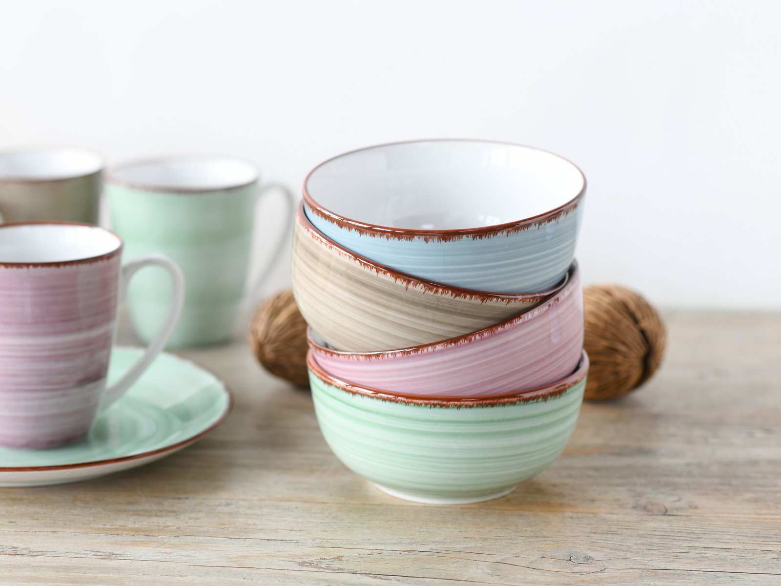 Stapel von vier bunten Schalen in Pastellfarben auf einem Holztisch, mit Tassen im Hintergrund, seitliche Perspektive