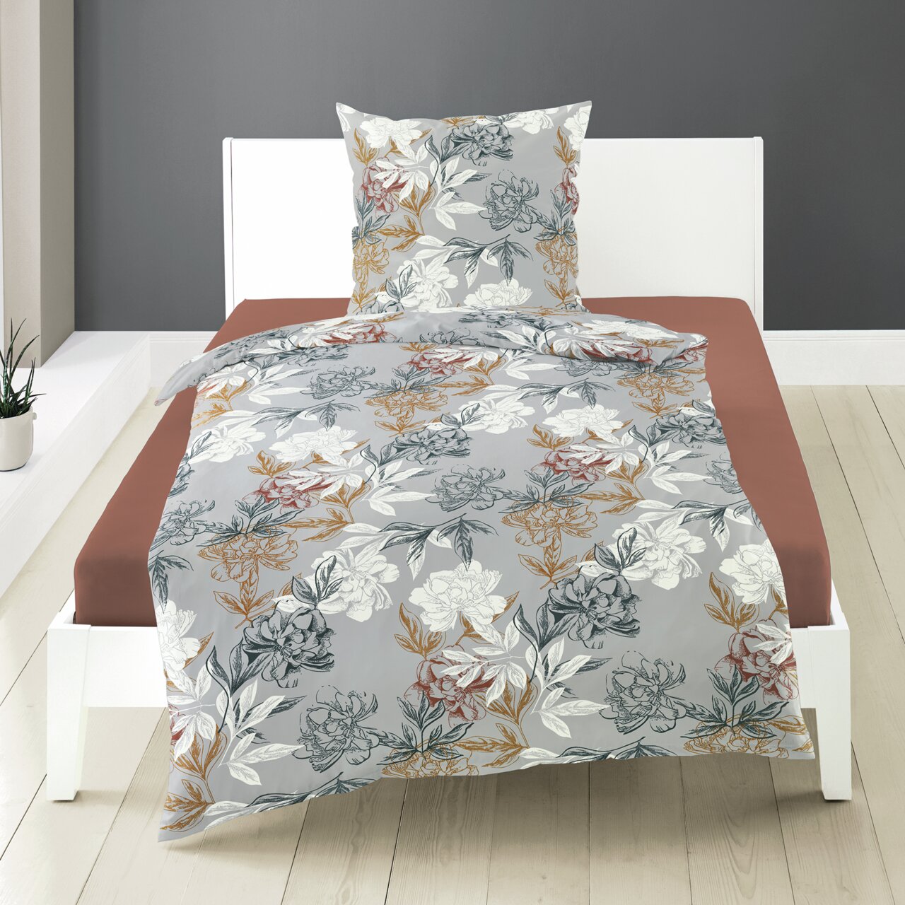 Beddengoedset van makosatijn met bloemmotief in grijs, wit en aardetinten, op een wit bedframe in een moderne slaapkamer, vooraanzicht