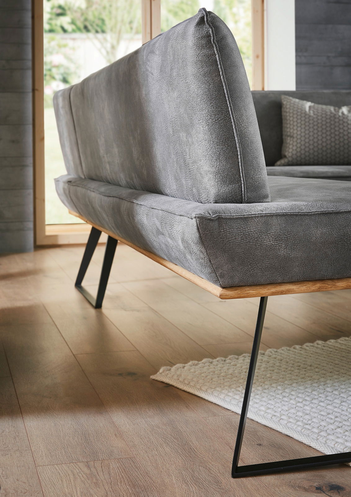 Voleo Eckbank MALIBU Graue Eckbank mit modernem Design, seitliche Perspektive, Metallbeine und Holzakzente, auf Holzboden stehend.