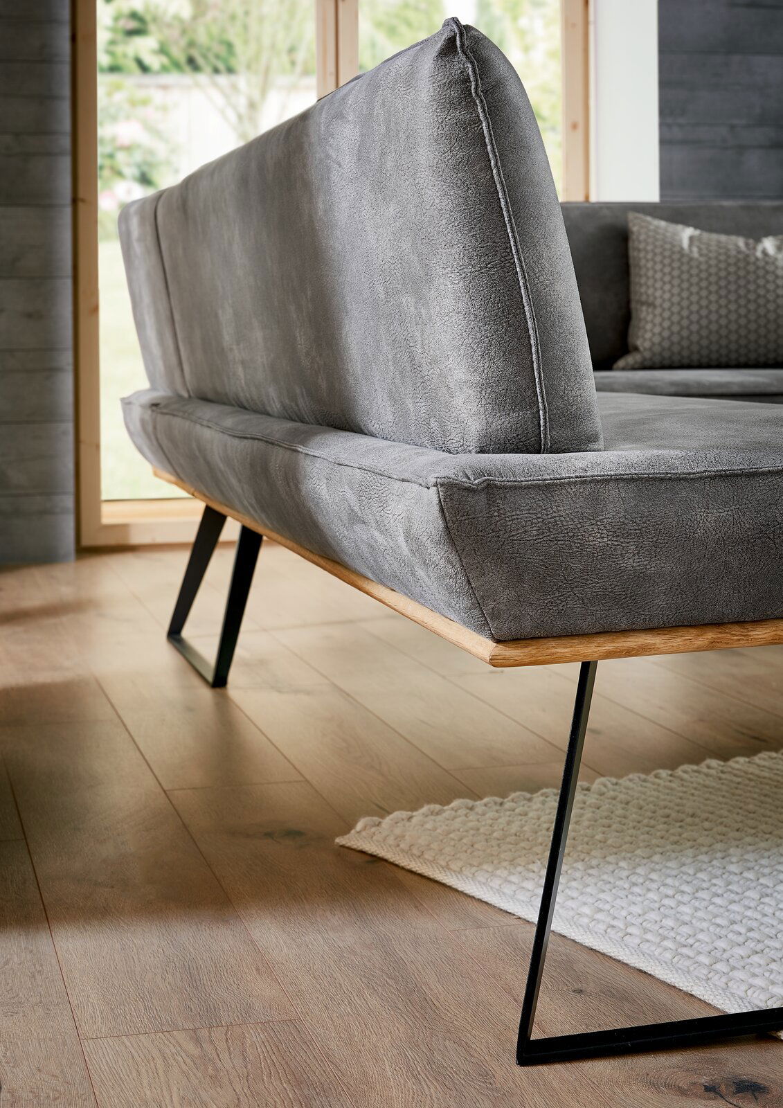 Voleo Eckbank MALIBU Graue Eckbank mit modernem Design, seitliche Perspektive, Metallbeine und Holzakzente, auf Holzboden stehend.