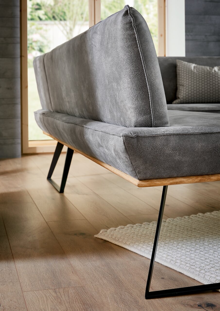 Voleo Eckbank MALIBU Graue Eckbank mit modernem Design, seitliche Perspektive, Metallbeine und Holzakzente, auf Holzboden stehend.