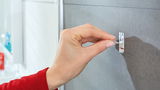 Nahaufnahme einer Hand, die einen tesa Powerstrip Waterproof an einer grauen Wand anbringt.